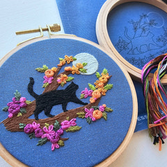 4 inch Embroidery hoop with a black cat and floral design on blue fabric, with another hoop and thread in the background.