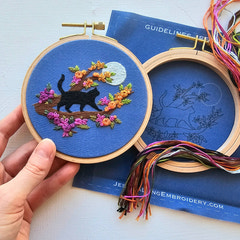 Embroidery hoop with a cat design on a blue background, held by a hand.