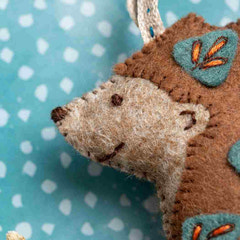 Close-up of a brown and beige hedgehog plush toy with a blue background. Designed by Corinne Lapierre. Available at tinypatio.com