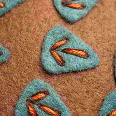 Close-up of green embroidered patches with orange stitching on a brown fabric background. Designed by Corinne Lapierre. Available at tinypatio.com
