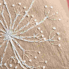 Close-up of embroidered design on fabric with white thread and beads.