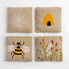 Four embroidered panels with bee, flower, and beehive designs on a beige background.