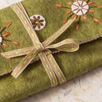 Green fabric with embroidered flowers and a ribbon on a light background. Designed by Corinne Lapierre. Available at tinypatio.com