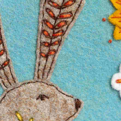 Close-up of a felted hare with embroidered details on a blue felt background. By Corinne Lapierre. Available at tinypatio.com