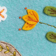 Felted yellow flower with red stamens on a textured blue felt background. By Corinne Lapierre. Available at tinypatio.com