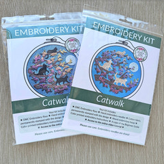 Two embroidery kits with cat-themed designs on a wooden surface. Beginner Embroidery kit with black cats and floral design on blue fabric. Designed by Jessica Long Embroidery. Curated by Tiny Patio in the UK. 