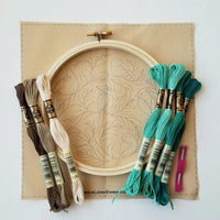 A picture showing supplies of Jessica Long Winter Birds Embroidery Kit, including 7 full skeins of DMC thread, pre-printed fabric, an embroidery hoop and embroidery needles