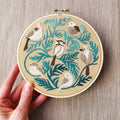 a hand holding a finished Jessica Long Winter Birds Embroidery Kit, the design features Beginner Chain Stitch, 6" Hoop
