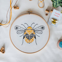 Finished bumblebee embroidery in an 8 inch wooden hoop, stitched in gold and black on pale organic cotton