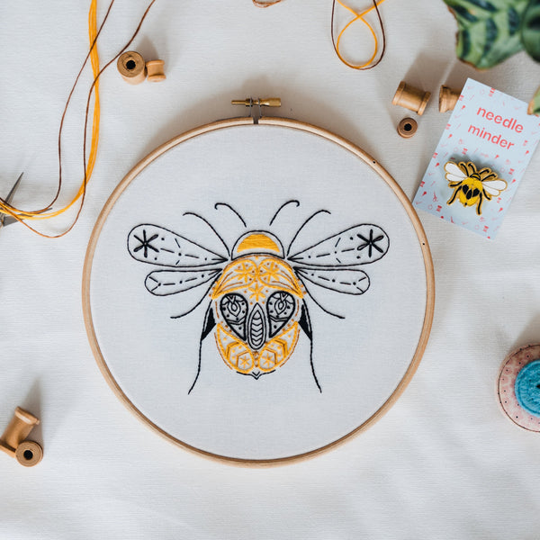 Finished bumblebee embroidery in an 8 inch wooden hoop, stitched in gold and black on pale organic cotton