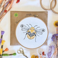 Paraffle kraft kit envelope with the completed bee hoop resting on it, DMC threads and scissors arranged around