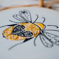 Close-up of the bee's gold paisley body and fine black wing outlines in stranded cotton