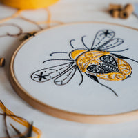 The bee hoop tilted against a bright background with loose gold thread trailing from it