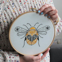 Someone in a knitted jumper holding up the finished bee hoop