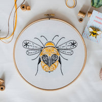The finished bee hoop flat on white beside wooden thread spools and a matching bee needle minder