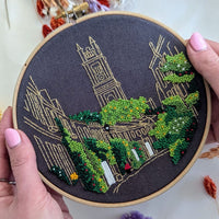 A hand holding the finished Circus Lane hoop, showing the church spire and cobbled street in gold thread