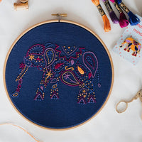 The elephant kit laid out flat with its wooden hoop, DMC threads and a needle minder packet