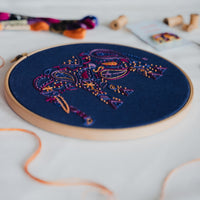 The elephant hoop tilted on a patterned rug with a trailing length of peach thread