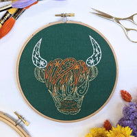 Finished Highland coo embroidery in a 6 inch wooden hoop, stitched in orange and cream on forest green fabric