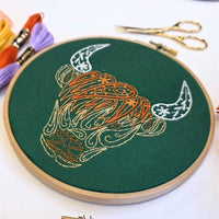 The Highland coo hoop photographed from above with skeins of DMC thread and embroidery scissors around it