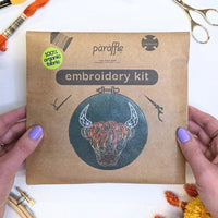 Hands holding the Paraffle kraft kit envelope, printed with the Highland coo design and an organic fabric sticker