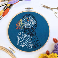 Finished paisley puffin embroidery in a 6 inch wooden hoop, stitched in white, black and orange on sea-blue fabric