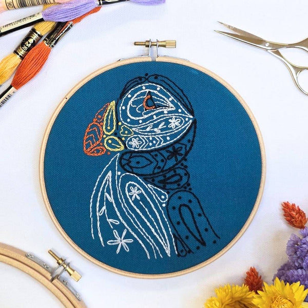 Finished paisley puffin embroidery in a 6 inch wooden hoop, stitched in white, black and orange on sea-blue fabric