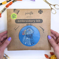 Hands holding the Paraffle kraft kit envelope printed with the puffin design