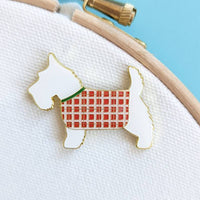 The Scottish terrier needle minder sitting on white hooped fabric, showing its gold-outlined enamel detail