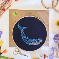 Paraffle kraft paper kit envelope with the finished navy whale hoop resting on top, DMC threads and scissors around it