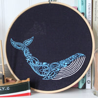 The whale embroidery hoop propped on a shelf beside a stack of books and a model boat